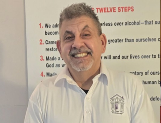 Recovery house member in front of a poster of the 12 Steps of Alcoholics Anonymous